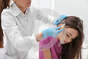 Doctor using nit comb on little girl`s hair indoors. Anti lice treatment photo