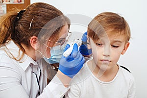 Doctor using otoscope to examine boy`s ear. Pediatrician examining little patient with otoscope. Child hearing exam