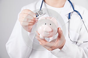 Doctor using stethoscope to piggy bank