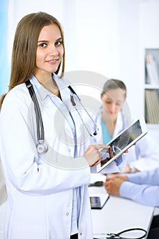 Doctor using tablet computer, close-up of hands at touch pad screen. Patient is at the background