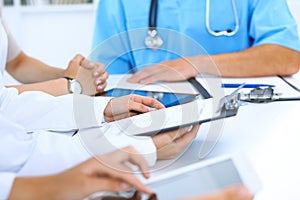 Doctor using tablet computer at medical meeting, closeup. Group of colleagues at the background