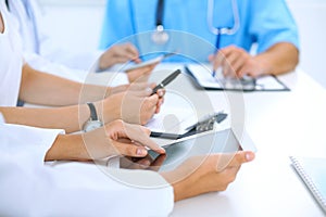 Doctor using tablet computer at medical meeting, closeup. Group of colleagues at the background