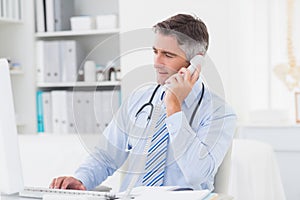 Doctor using telephone while working on computer