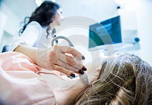 Doctor using ultrasound scanning machine for examining a thyroid of woman