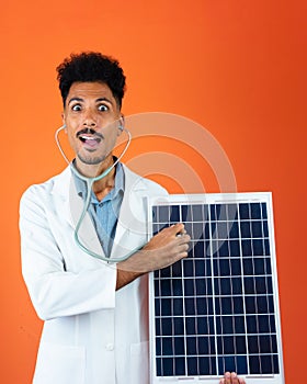 Doctor or Veterinarian Isolated on Orange Background. Black Young Doctor Medical Resident With Stethoscope Holding Solar Panel