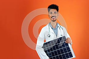 Doctor or Veterinarian Isolated on Orange Background. Black Young Doctor Medical Resident With Stethoscope Holding Solar Panel