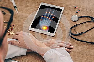 Doctor watching a digital tablet with x-ray of a right hand with osteoarthritis pains on the joints of the fingers and wrists.
