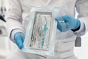 Doctor Wearing Blue Sterile Gloves Demonstating Sealed Sterilization Pouch With Dental Tools