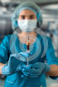 doctor wearing blue uniform with glove full virus protection holding syringe with medicine