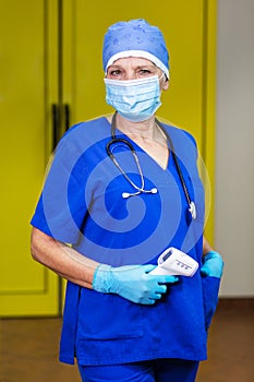 A doctor wearing a blue uniform and protective medical accessories with a non-contact thermometer