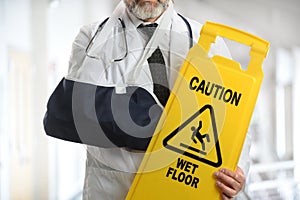 Doctor Wearing Elbow Sling Holding Caution Sign