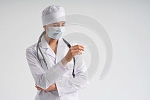 Doctor wearing face mask looking at measurement on medical thermometer over white background