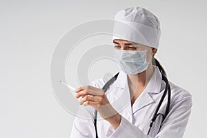 Doctor wearing face mask looking at measurement on medical thermometer over white background with copy space