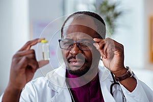 Doctor wearing glasses looking at ampoule checking the liquid