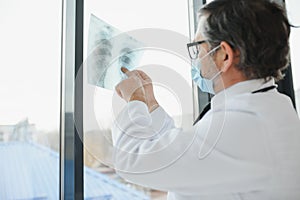 Doctor wearing mask and looking at chest x-ray.
