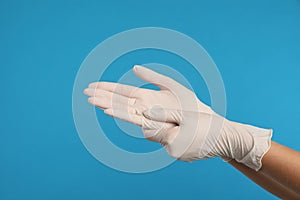 Doctor wearing medical gloves on light blue background, closeup