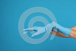 Doctor wearing medical gloves on light blue background, closeup. Space for text