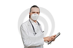 A doctor wearing a medical mask points at the blank black screen of the tablet.