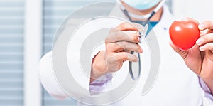 doctor wearing white coat standing holds his stethoscope on hand for listening examining red heart