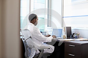 Doctor Wearing White Coat Working On Laptop In Office