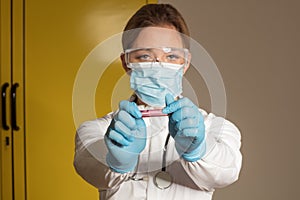 Doctor wearing a white overall and goggles holding a test tube