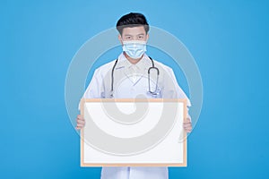 doctor wears a surgical mask holding an empty whiteboard horizontally