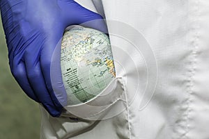 a doctor in a white coat and blue gloves puts a globe of the globe concept healthcare pharmaceuticals in the pocket of