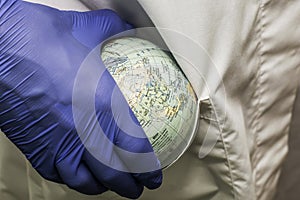 a doctor in a white coat and blue gloves puts a globe of the globe concept healthcare pharmaceuticals in the pocket of