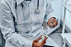 A doctor in a white coat draws the vaccine with a syringe from a vial. Vaccination. Cropped image