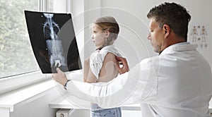 Doctor in white coat examines girl`s back and shows X-ray in hospital