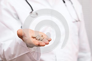 Doctor in a white coat holding pills in a hand