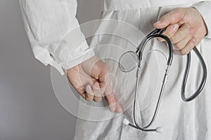 Doctor in white coat holds hands behind his back with stethoscope. Close up.
