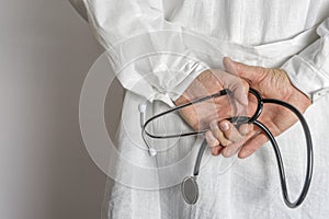 Doctor in white coat holds hands behind his back with stethoscope. Close up.