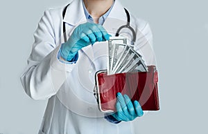 Doctor in white coat holds red purse with dollars in hands and takes money