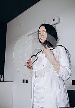 doctor in a white coat holds a stethoscope in his hand on a white background, close-up.