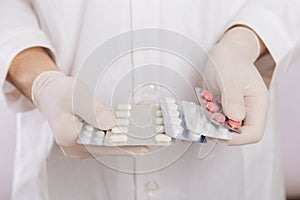 A doctor in a white coat, a medical mask and gloves holds pills. Types of drugs. Medical worker on a white background. Studio