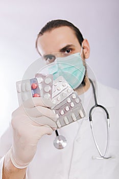 A doctor in a white coat, a medical mask and gloves holds pills. Types of drugs. Medical worker on a white background. Studio