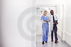 Doctor In White Coat And Nurse In Scrubs Looking At Digital Tablet In Hospital Corridor