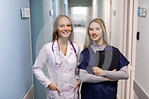 Doctor In White Coat And Nurse In Scrubs Looking At Digital Tablet In Hospital Corridor