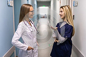 Doctor In White Coat And Nurse In Scrubs Looking At Digital Tablet In Hospital Corridor