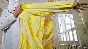 A doctor in a white coat puts on a yellow protective suit for work in an epidemic and pandemic. The corridor of the hospital.