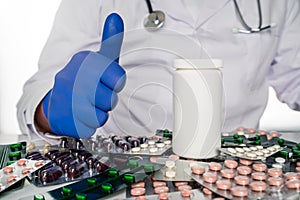 Doctor in white coat sits infront of pill boards scattered on table giving thumbs up next to blank prescription bottle.