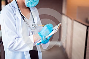 Doctor in white coat with stethoscope and blue glove write report by pencil in a notebook on hand at hospital.