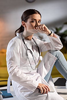 Doctor in white coat with stethoscope holding smartphone during night shift
