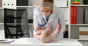 Doctor in white lab coat listening to baby in stethoscope.