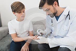 The doctor in white medical gloves takes the boy`s blood sample to the level of sugar.