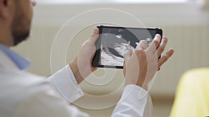 Doctor in white medical robe shows pictures of ultrasound to pregnant woman on a tablet