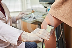 Doctor in white uniform with diagnostic equipment performs an ultrasound examination of leg veins of a female patient.