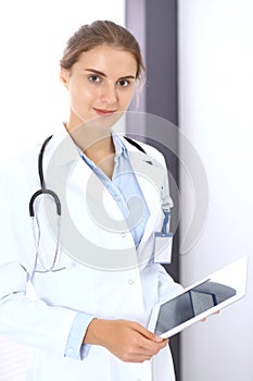 Doctor woman in clinic office. Female physician at work using digital tablet while standing straight at hospita