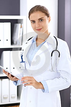 Doctor woman in clinic office. Female physician at work using digital tablet while standing straight at hospita